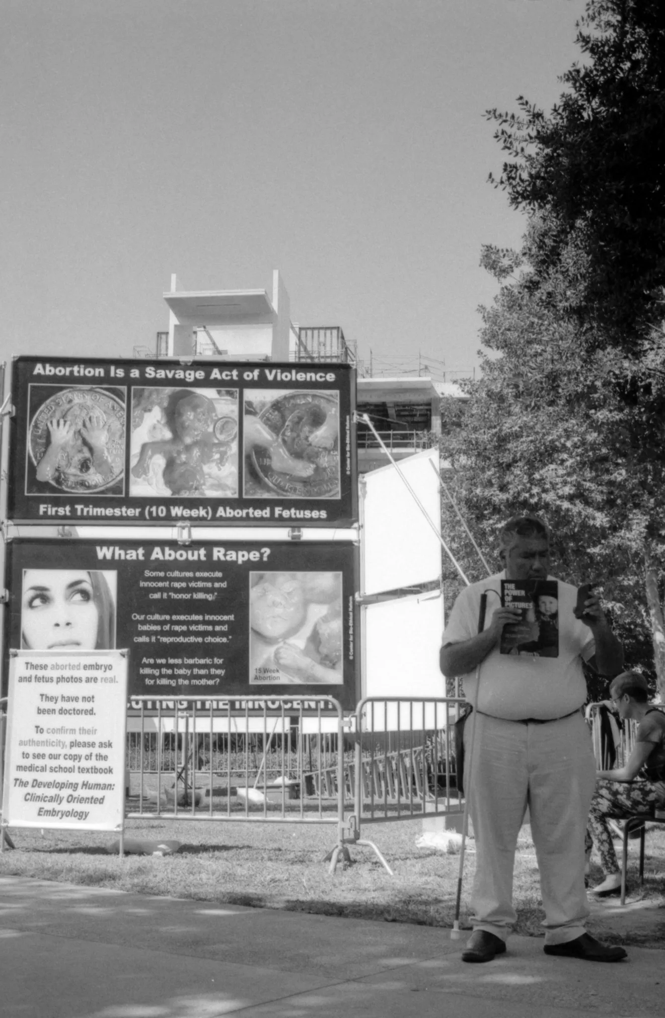 A photo of a blind man with anti-abortion papers. He is pointing to nothing