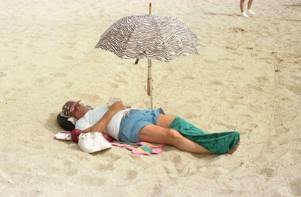 A man sleeping on the beach, covered by an umbrella