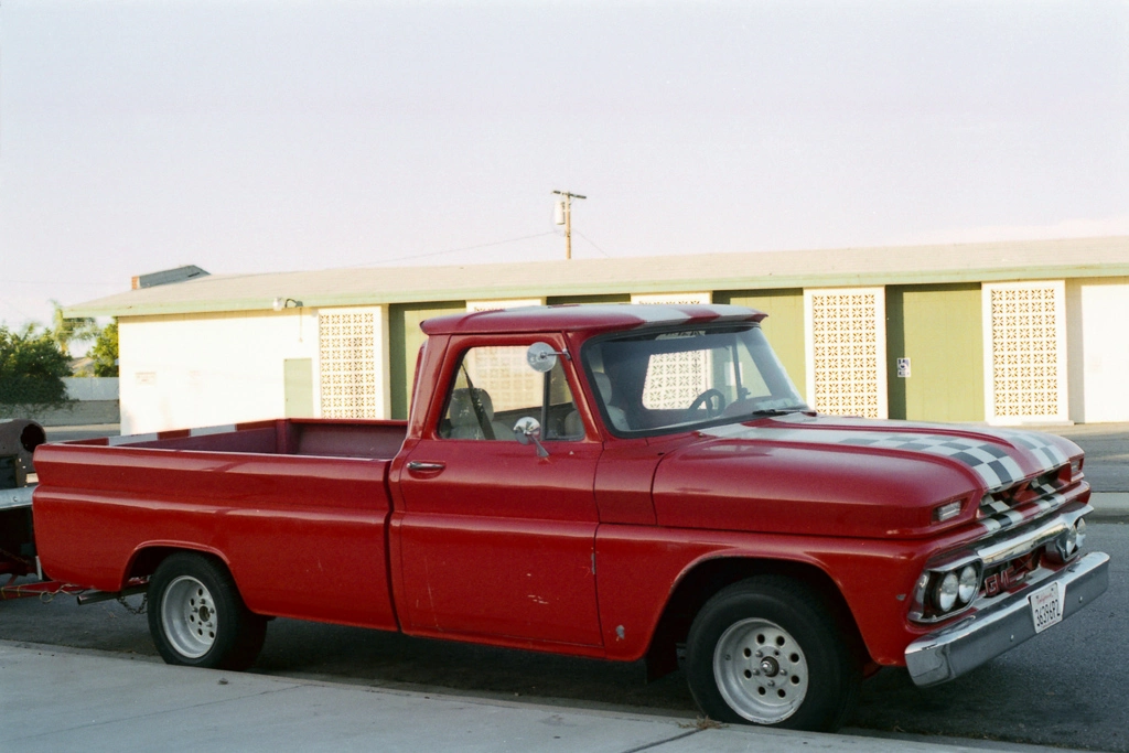 A bright red truck with two black and white stripes going down the hood.